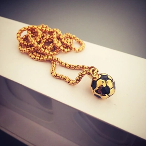 Dettaglio di un ciondolo da calcio bicolore oro e nero su una catena a maglie box