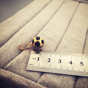 Dettaglio ciondolo calcio dorato da 13mm su velluto grigio con riferimento scala