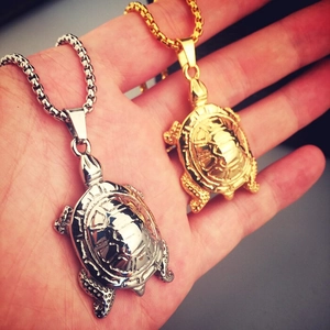 Détail de pendentifs tortue hiphop en or et argent tenus dans la main