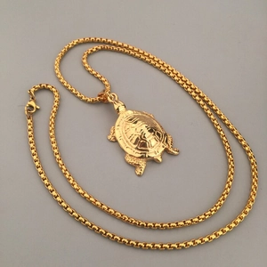 Détail du pendentif tortue doré avec sa chaîne à mailles vénitiennes sur fond neutre
