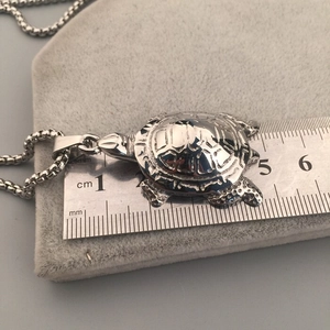 Détail du pendentif tortue argentée avec règle en acier pour mesurer la taille exacte
