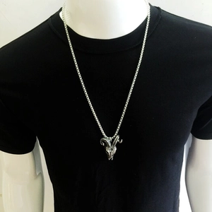 Detailed close-up of a vintage silver ram head pendant on a black shirt background