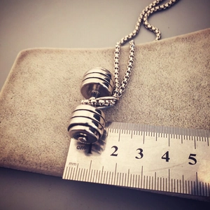 Colgante de mancuerna plateada sobre fieltro gris con regla para referencia de talla