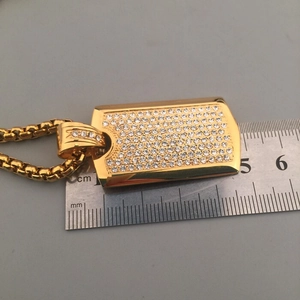 Macro detail of iced-out gold rectangle pendant with dimensions shown on a ruler