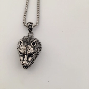 Detailed close-up of a silver wolf head pendant with textured fur and woven steel chain