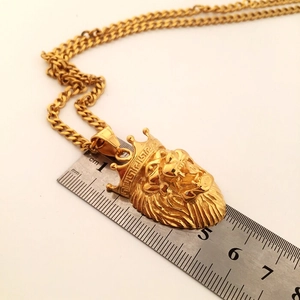 Detail shot of golden lion head pendant with crown showing dimensions with a ruler