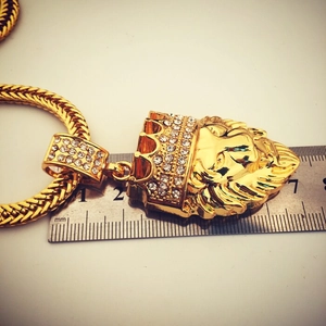 Golden crown lion head pendant with white rhinestones measured against a metric ruler