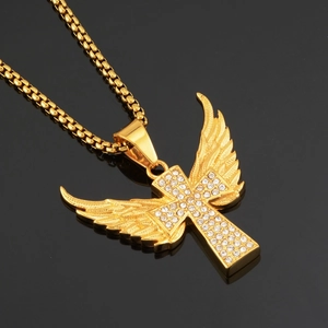 Vue macro d'un pendentif croix ailée dorée serti de strass blancs sur fond noir miroir