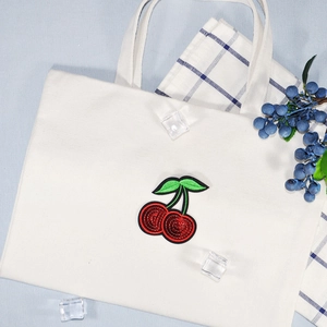 White canvas tote bag featuring a high-quality red cherry embroidery patch on a blue background