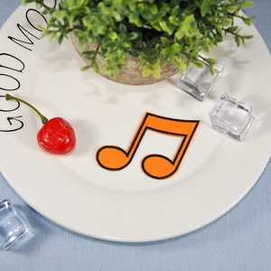 Vibrant orange music note embroidery patch with black edges on a white plate