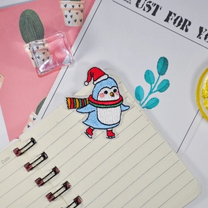 Embroidered Christmas penguin patch with Santa hat and scarf on stationery background