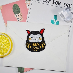 Cartoon Daruma embroidery patch with golden character on white envelope background