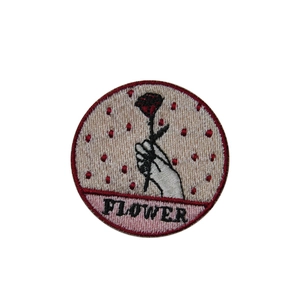 Embroidered round patch featuring a flower design and bold text on a beige dotted background