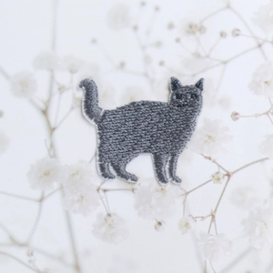 Toppa ricamata gatto grigio dettagliata con bordo bianco su sfondo floreale decorativo