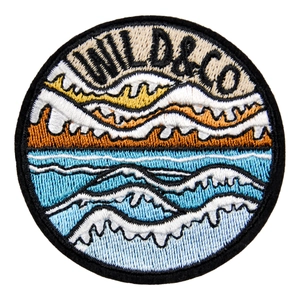 Round embroidered patch featuring mountains and ocean waves with WILD & CO text
