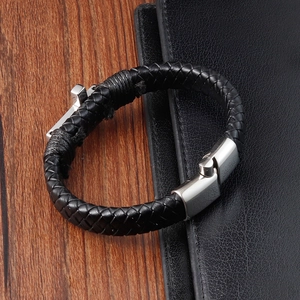 Detail of men's black braided leather bracelet with silver steel cross and magnetic clasp