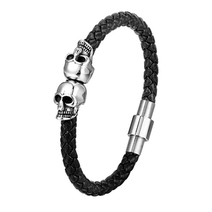 Macro detail of black braided leather bracelet with silver skull charms and magnetic clasp