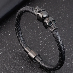 Men's braided black leather bracelet featuring dual metal skull motifs and a magnetic clasp