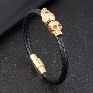 Men's woven black leather bracelet featuring two golden skull charms and magnetic clasp