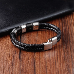 Close-up of black braided leather men's bracelet with metal charms on wood surface