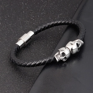Macro view of men's black braided leather bracelet featuring dual polished metal skulls