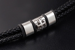 Detail view of black braided leather bracelet featuring a silver cross metal charm