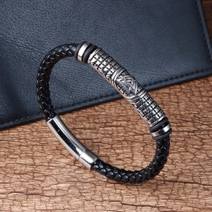Detail des geflochtenen schwarzen Lederarmbands mit graviertem Metallverschluss auf Holz
