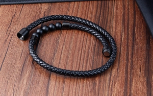 Detail view of woven black leather strap and matte volcanic stone beads on male bracelet