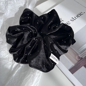 Elegant black velvet scrunchie with silver sparkles and a handmade label on a minimal background