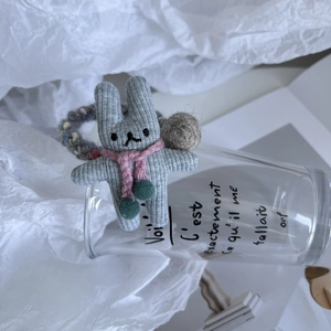 Détail d'un chouchou lapin gris tricoté main avec écharpe rose et petits pompons