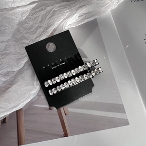 Detail view of two minimalist rhinestone hair clips on a black branded display card