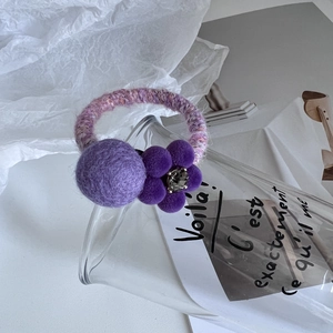 Détail d'un chouchou en peluche violette avec fleur tricotée et boules en feutre