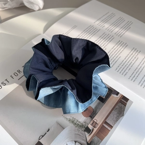 Detailansicht eines zweifarbigen Denim-Haargummis mit Faltenstruktur auf Magazin