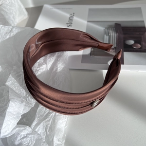 Close-up of brown satin wide headband featuring a polished silver metal logo disc