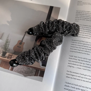 Fermaglio a banana plissettato con strass brillanti su sfondo di libro d'epoca