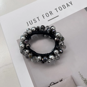 Détail d'un chouchou élastique avec perles argentées et cristaux gris sur fond de magazine
