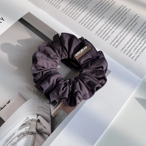 Détail d'un chouchou plissé en tissu violet foncé avec étiquette de marque tissée