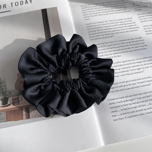 Macro shot of black satin scrunchie showing glossy texture and elegant fabric folds