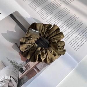 Gros plan d'un chouchou en tissu vert olive avec étiquette sur fond de magazine esthétique