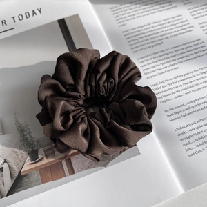 Close-up of a coffee brown satin hair scrunchie placed on an open book with soft light