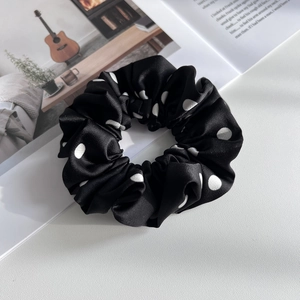 Detailed view of large black satin hair scrunchie with white polka dots on a white surface