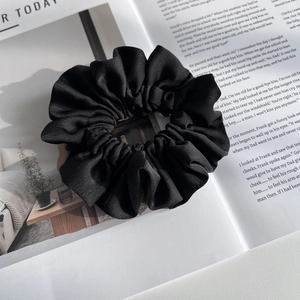 Detailed view of a black satin scrunchie styled on a fashion magazine background