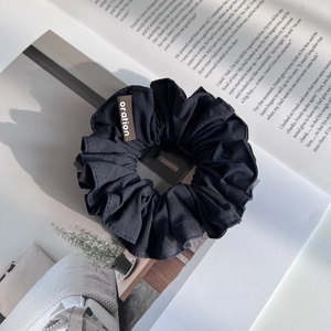 Détail d'un chouchou en tissu noir avec étiquette tissée marron sur fond de magazine