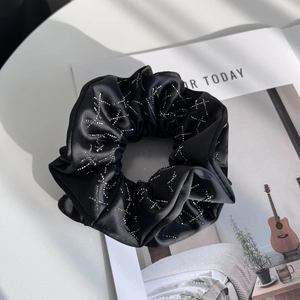 Vue détaillée d'un chouchou en satin noir orné d'étoiles en strass sur une table blanche