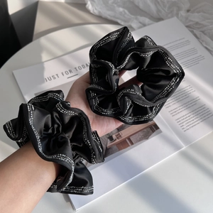 Dettaglio di due elastici scrunchie in raso nero con ricamo di perline argentate