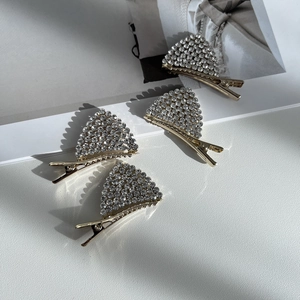Détail de quatre barrettes triangulaires dorées ornées de strass sur fond blanc élégant