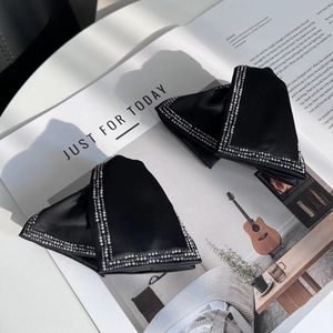 Detail of two black satin bow hair clips with pearl edge on a magazine with text