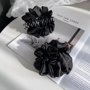 Detail of black satin flower hair claw clip with rhinestone edge on a magazine background