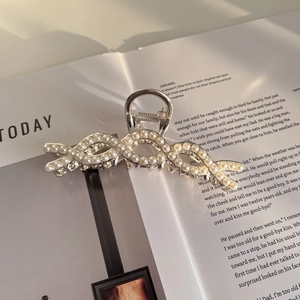 Detailweergave van de zilveren haarklem met elegante witte parels op een boekachtergrond