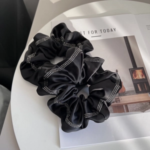 Detail of two black satin scrunchies with elegant rhinestone stripes on magazine background